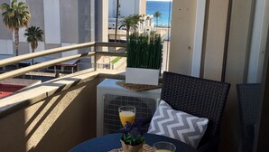 Un balcon avec une table dressée pour deux personnes, agrémenté d’un journal, d’un verre de jus d’orange et d’une plante en pot.