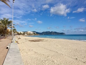 A wide sandy beach with a clear blue sky and distant mountains.
