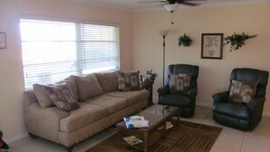 Un salon avec un canapé beige, deux fauteuils, une table basse, un lampadaire et un ventilateur de plafond.