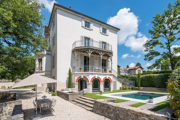 A two-story building with a balcony, a swimming pool, and a patio area with outdoor furniture.