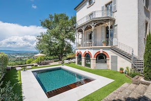 A pool with a wooden deck, a balcony with outdoor furniture, and a view of the countryside.