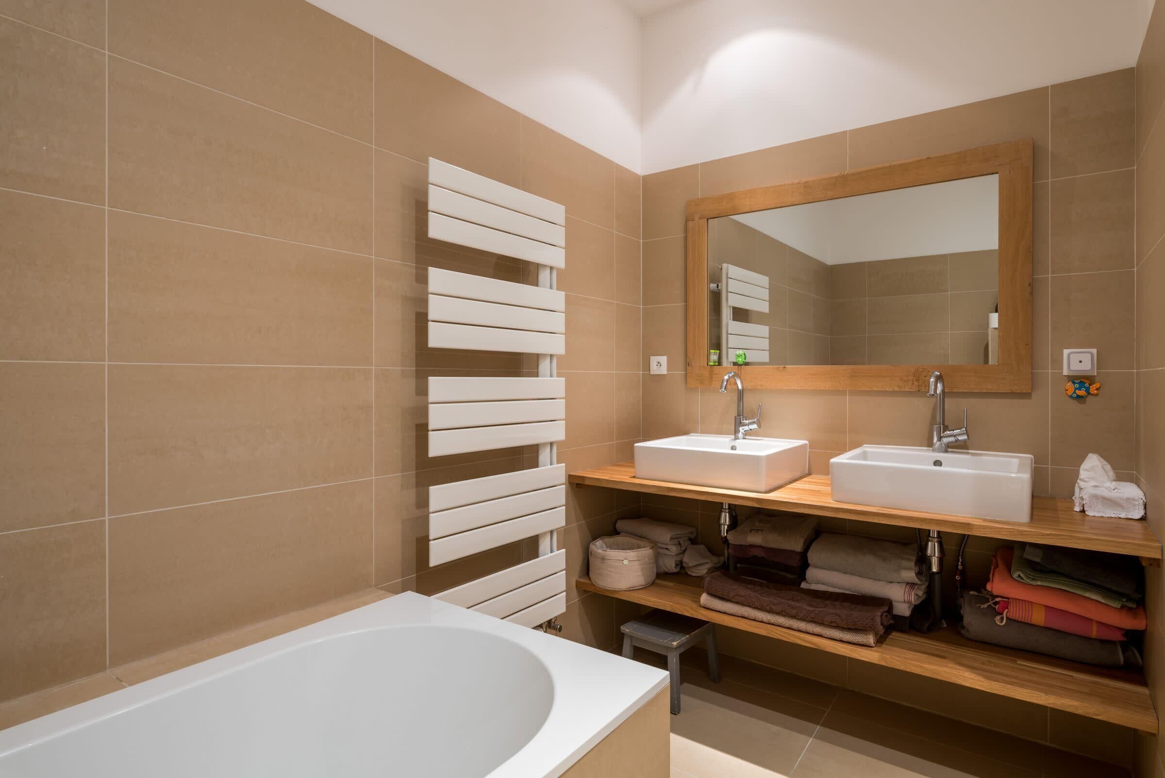 Un baño moderno con bañera, dos lavamanos, un espejo grande y espacio para toallas.