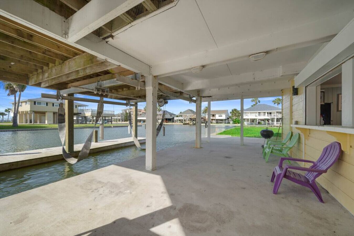 A covered outdoor area with concrete flooring, a water body in the background, and a few chairs.