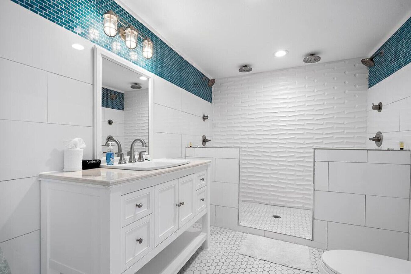 A modern bathroom with a white vanity, a large mirror, a shower with a textured wall, and a hexagonal tile floor.