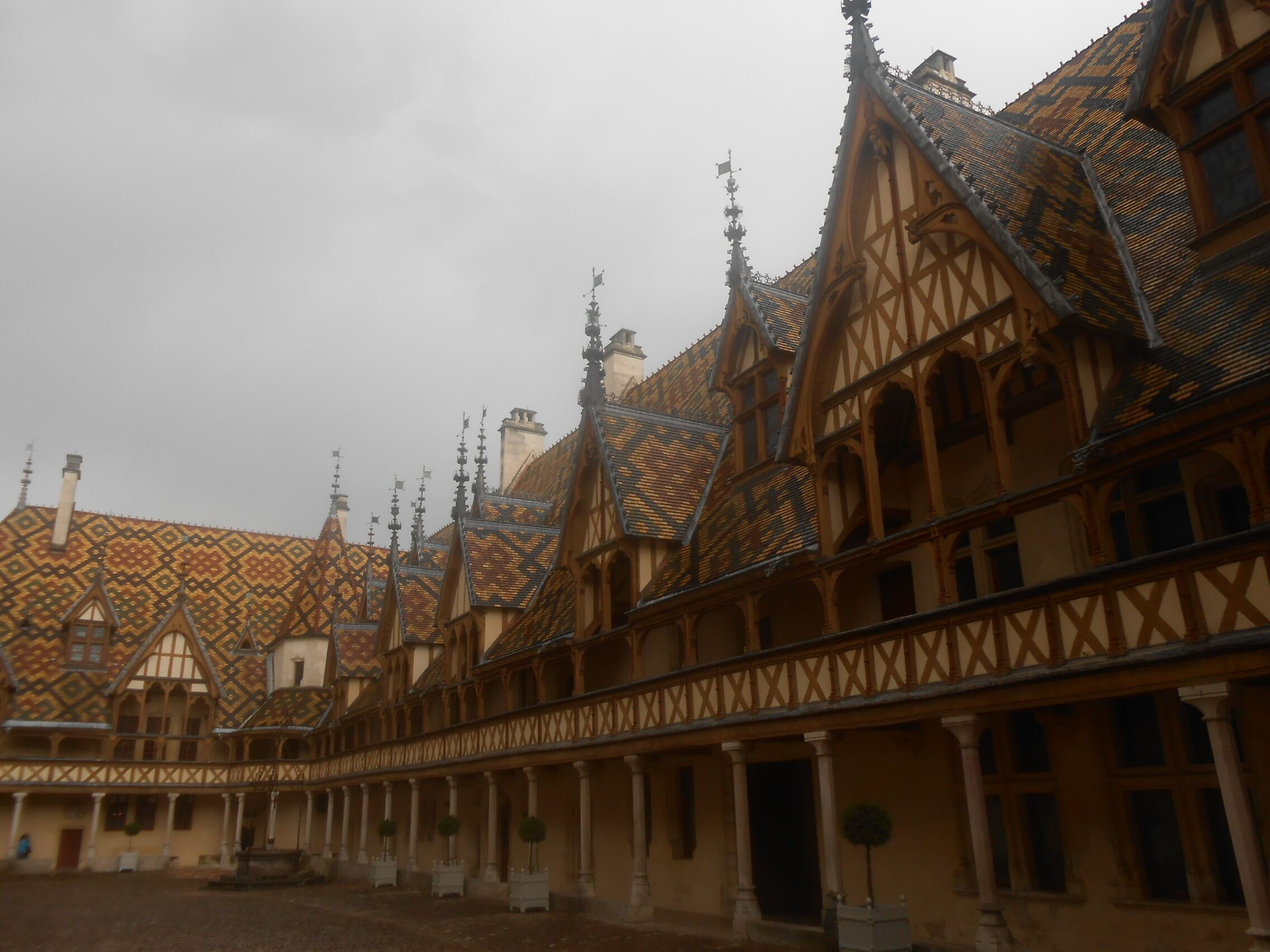 Une cour bordée de bâtiments traditionnels à colombages, une allée couverte et une fontaine centrale.