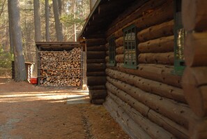 A log cabin with a stack of firewood and a window with green shutters.