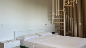 Une chambre avec un lit simple, une table de chevet, une lampe fixée au mur et un escalier en colimaçon.