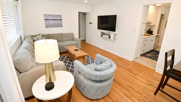 A modern living room with a sofa, a coffee table, a lamp, a television, and a dining area with a chair. - Remodeled home 1 mile from Notre Dame (1150) (South Bend)