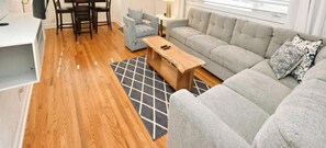 Un salon moderne avec un canapé gris, une table basse en bois et un coin repas comprenant des chaises et une table.