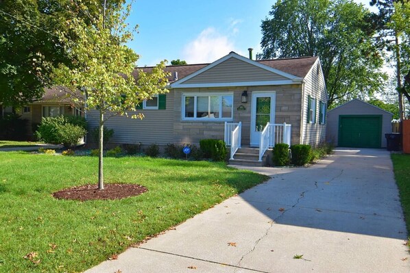 A single-story house with a front porch, a driveway, and a green garage door.