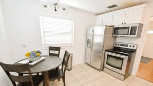 A compact kitchen with a refrigerator, microwave, and oven. There is a dining table with chairs and a vase of flowers. - Remodeled home 1 mile from Notre Dame (1150) (South Bend)
