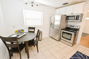 A compact kitchen with a refrigerator, microwave, and oven. There is a dining table with chairs and a vase of flowers. - Remodeled home 1 mile from Notre Dame (1150) (South Bend)