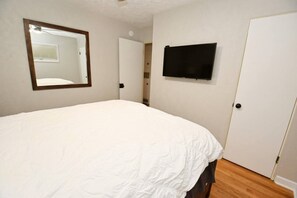 Een slaapkamer met een groot bed, een wandtelevisie en een deur naar een andere kamer.