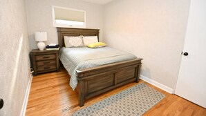 A bedroom with a wooden bed, a nightstand, a lamp, a ceiling fan, and a door. - Remodeled home 1 mile from Notre Dame (1150) (South Bend)