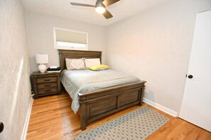 A bedroom with a wooden bed, a nightstand, a lamp, a ceiling fan, and a door. - Remodeled home 1 mile from Notre Dame (1150) (South Bend)