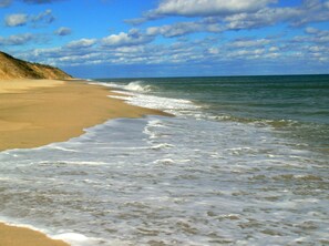 Een strand met golven die op het strand komen, een heldere lucht en een zandig landschap.