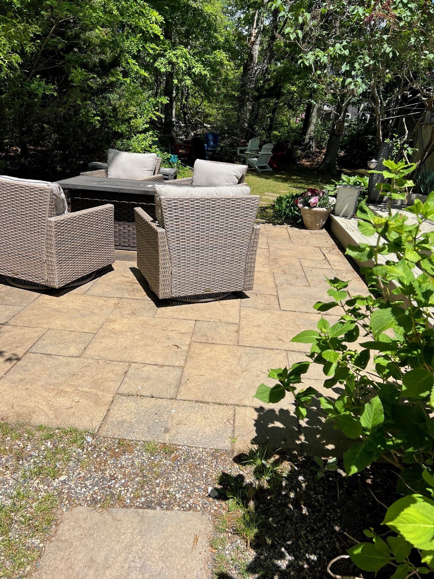 An outdoor patio with wicker furniture, a stone floor, and surrounding greenery.