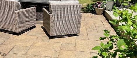 An outdoor patio with wicker furniture, a stone floor, and surrounding greenery.