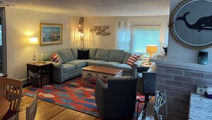 Ein gemütliches Wohnzimmer mit Ecksofa, Couchtisch, Kamin und einer Wanddekoration im Seestil.