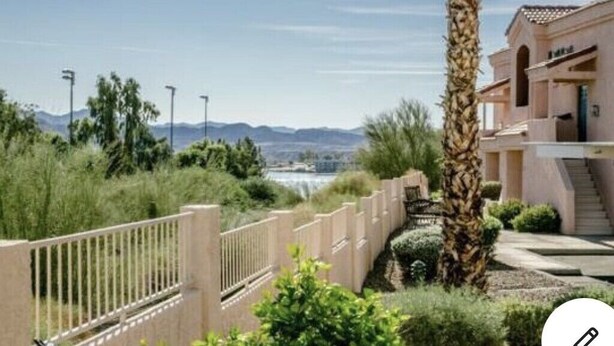 Zona residencial con entrada protegida por un muro, una palmera y un edificio de fachada clara.