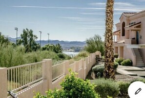Zona residencial con entrada protegida por un muro, una palmera y un edificio de fachada clara.