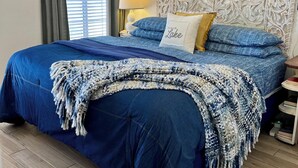 Un dormitorio con una cama grande, un cabecero decorativo, una mesita de noche con lámpara y una ventana con cortinas.