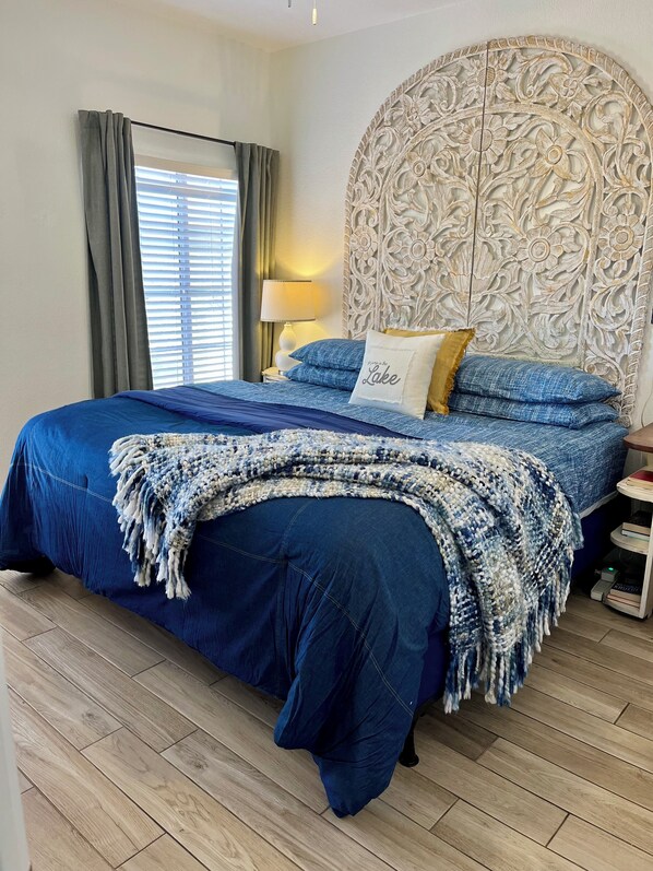 A bedroom with a large bed, a decorative headboard, a bedside table with a lamp, and a window with curtains.