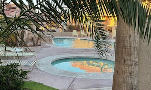 A pool area with two pools, lounge chairs, and palm trees. - Lakeshore Village “Classic Condo” 2 patios Prime Location (Lake Havasu City)