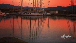 A marina with multiple sailboats docked, calm water reflecting the boats, and a sunset sky. - Cozy rooms to rent in Olbia City Center (Olbia)