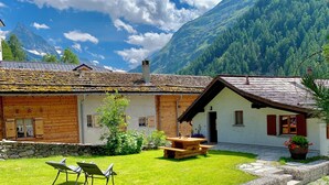 Una cabaña con pared de piedra, fachada de madera y patio césped con mobiliario de exterior.