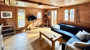 Interior de una cabaña de madera con piso de madera, un sofá, un televisor y una chimenea.