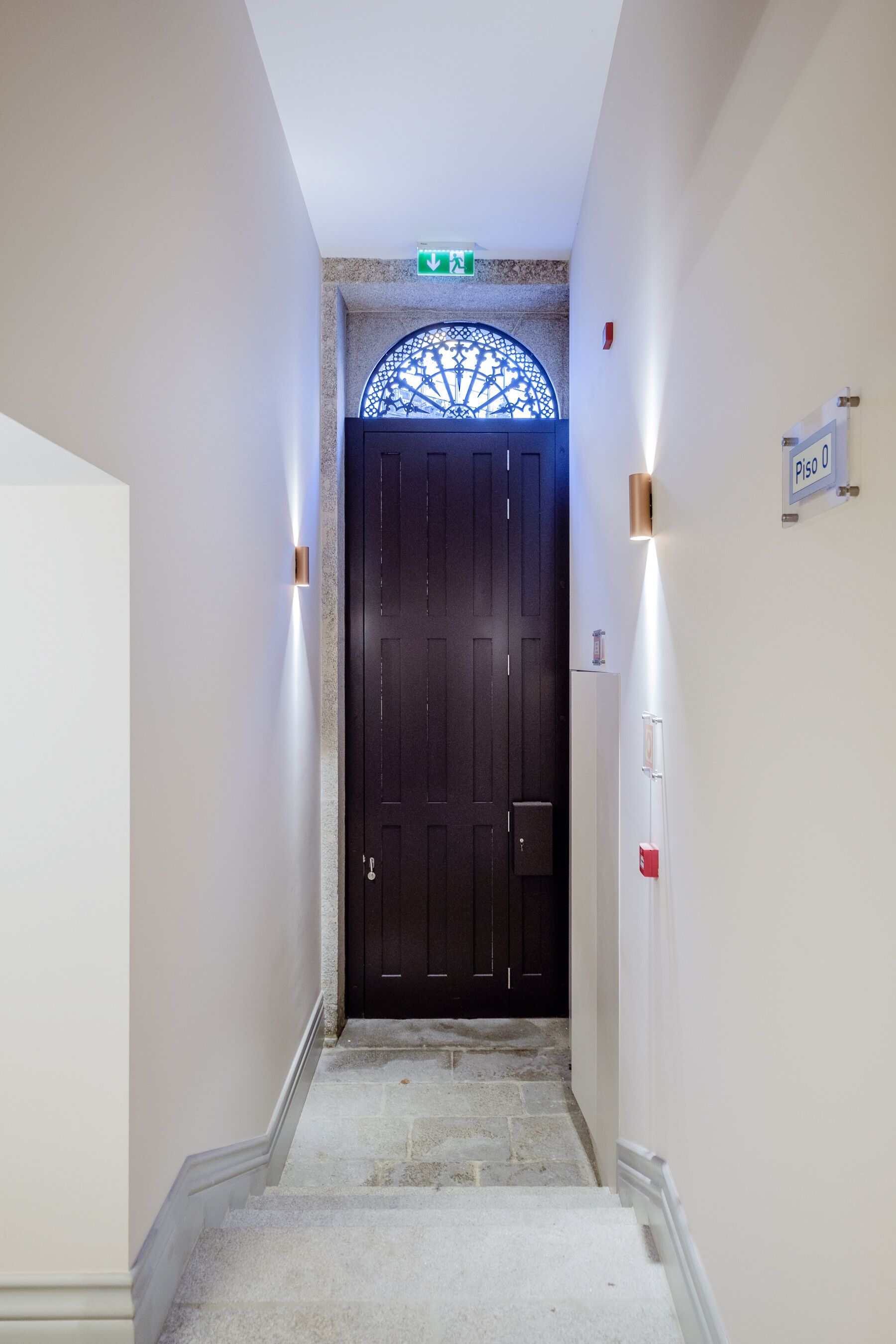 Un couloir avec une porte en bois sombre, un luminaire et une pancarte indiquant le numéro de la pièce.