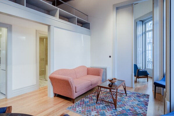 A modern living room with a pink sofa, a glass coffee table, and a patterned rug.