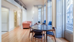 A spacious room with a round table and chairs, a sofa, and a large window with a view of buildings.