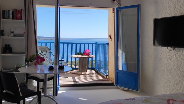 Un balcón con mesa y sillas, un televisor montado en la pared y vista al mar.