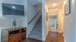 A modern living room with a flat-screen TV, wooden entertainment unit, and a staircase leading to another room.