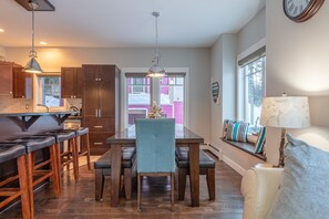A modern kitchen with wooden cabinets, a dining area with a bench, and a window with a view of a pink building.