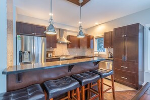 A modern kitchen with stainless steel appliances, dark wooden cabinets, and a bar area with leather stools.