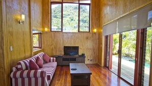 Ein großzügiges Wohnzimmer mit einem großen Fernseher, Holzwänden und einer Glastür, die auf eine Terrasse führt.