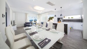 A modern dining area with a white table set for four, a kitchen in the background, and a view of the outdoors. - Luxury Villa Blue Silk with Heated Pool (Makarska)