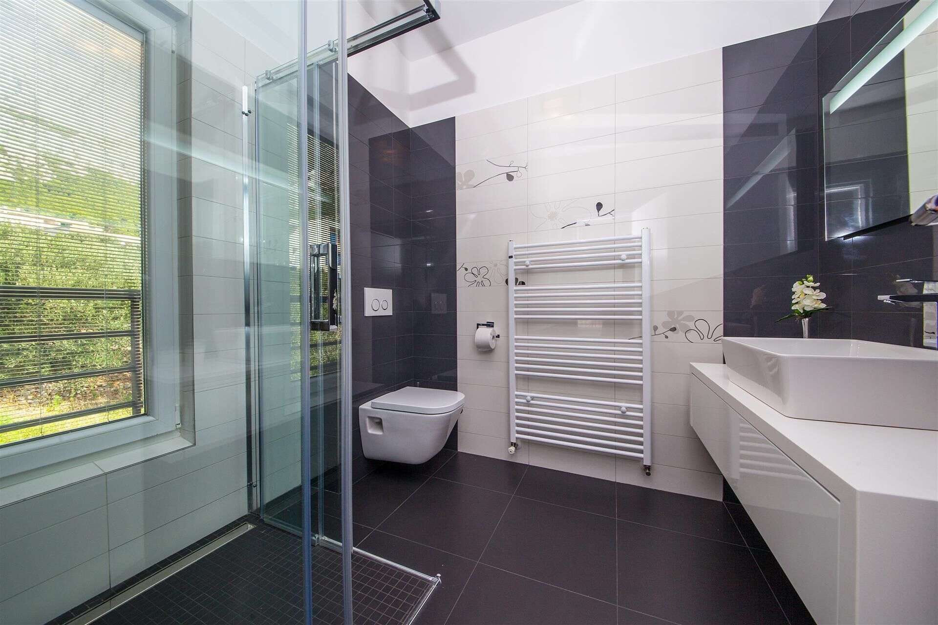 Une salle de bain moderne avec une douche à parois de verre, des toilettes blanches, un lavabo blanc et un porte-serviettes.