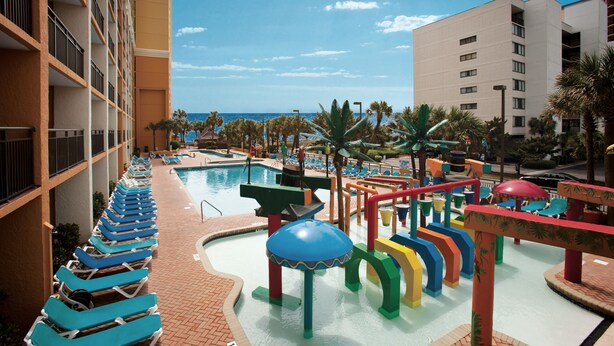 A resort pool area with a water slide, lounge chairs, and a view of the ocean.