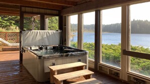 Un jacuzzi en una terraza de madera con escalones que llevan a él, con vista a un lago.