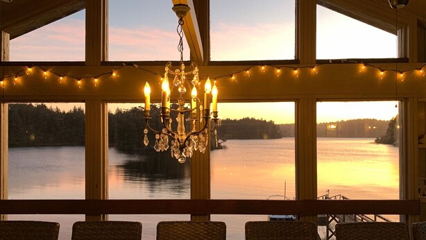 Comedor con vista a un lago al atardecer, con candelabro y luces colgantes.