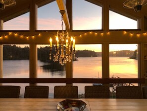 A dining area with a view of a lake at sunset, featuring a chandelier and string lights. - Luxurious Lake-Front Home with kayaks, SUPS, boat dock, hot tub, pool table... (Langlois)