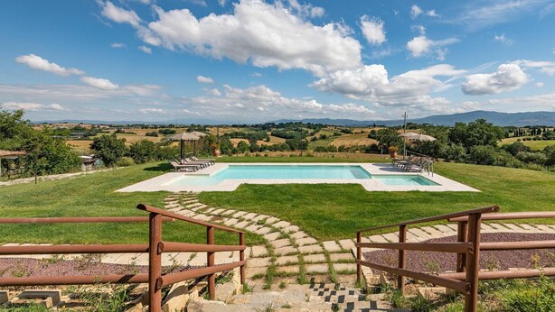 Piscina con vistas al campo, rodeada por una valla de madera y escalones que bajan al área de la piscina.