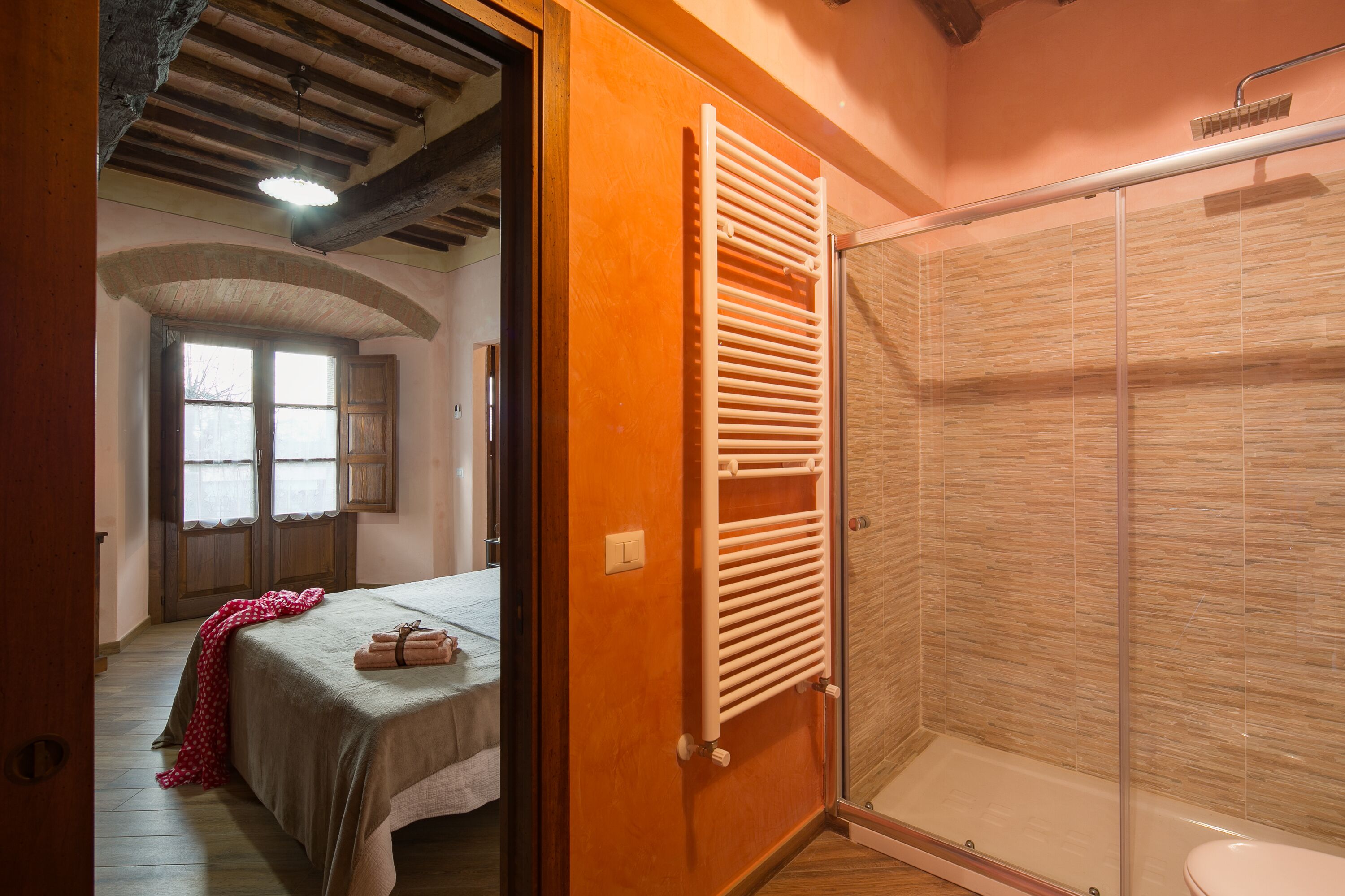Une chambre avec un lit, une porte en bois, un porte-serviettes et un espace douche dont les murs sont recouverts de carreaux.