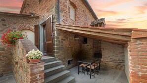 Un edificio rústico de piedra con fachada de ladrillo, una escalera de madera que conduce a un espacio exterior cubierto con una mesa y sillas.