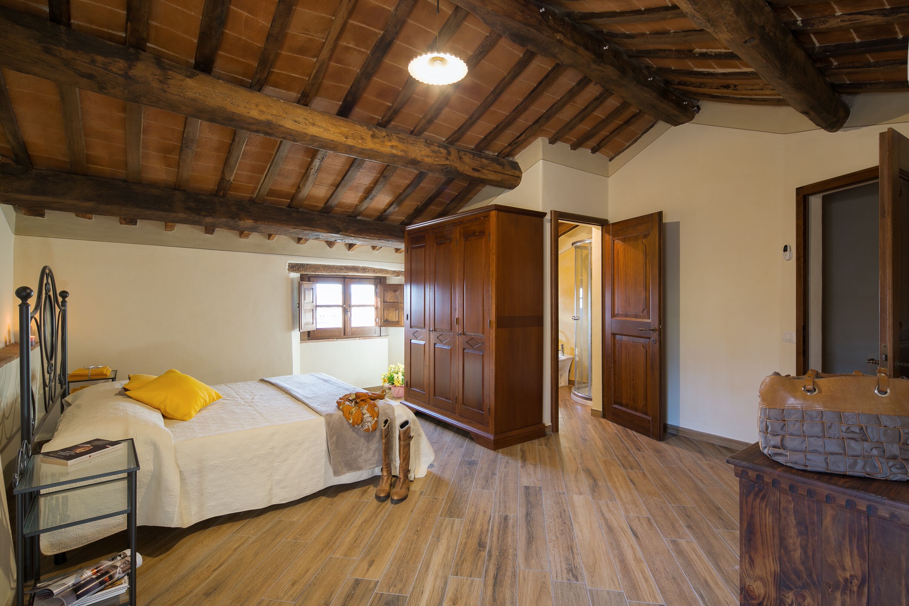 Une chambre avec un plafond en bois, un lit avec un oreiller jaune, une armoire en bois et une valise posée sur une commode.