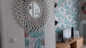 Un salon moderne avec un panneau décoratif au mur, un téléviseur posé sur un meuble en bois et une horloge accrochée au mur.